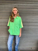 Camisa verde manzana de hilo de algodón, corte holgado, con cuello clásico, cierre frontal con botones, mangas cortas con doble raya amarilla y bolsillos de parche en el pecho.