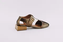 Sandalias de cuero color bronce, con diseño de punta cuadrada, taco cuadrado símil madera y tira ajustable con hebilla en el tobillo.