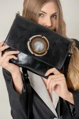 Sobre de cuero negro con solapa frontal decorada con una piedra de ágata natural en el centro. Cuenta con correa ajustable y extraíble, y cierre en la parte trasera.