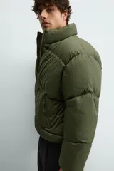 Cazadora acolchada tipo puffer de corte relajado, color verde militar. Presenta cuello subido, cierre frontal con cremallera, bolsillos laterales con cierre y puños elásticos.