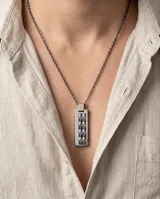 Collar de cadena de eslabones oscuros con dije rectangular de acero y detalles en cerámica con textura geométrica.
