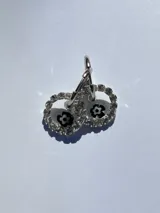 Aros colgantes plateados con dije circular de resina transparente con borde de strass y flor negra en el centro. El arito es de acero quirúrgico.