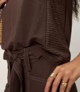 Blusa sin mangas color marrón, con escote redondo y corte recto. Presenta paneles laterales en tejido texturizado con rayas y una abertura vertical en la espalda con cierre discreto.