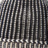 Gorro de lana con diseño de rayas verticales en blanco y negro, con borde doblado y pompón superior de pelo sintético negro.