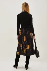 Falda midi plisada de color negro con estampado floral en tonos amarillos y detalles de efecto tie-dye. Presenta una silueta acampanada con movimiento y cintura elástica.