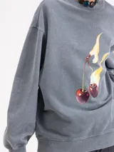 Buzo de algodón color gris con calce holgado, cuello redondo y mangas largas. Presenta un estampado frontal de cerezas con llamas y logo bordado en la espalda.