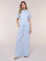 Conjunto de dos piezas confeccionado en lino, de estilo casual safari. Incluye camisa de manga corta con cuello camisero con bordado festoneado, abotonadura frontal y bolsillos en el pecho; y pantalón palazzo de tiro alto con bolsillos y cinturón con hebilla metálica dorada.