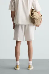 Bermuda de algodón color blanco, de corte relajado (relaxed fit), con cintura elástica ajustable mediante cordón. Posee bolsillos laterales y un bolsillo trasero de plastrón. Presenta un bordado en contraste en la pernera.