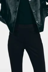 Pantalón de tiro alto confeccionado en punto roma, con diseño ajustado en la parte superior y piernas acampanadas. Presenta bolsillos insertados decorativos en la parte frontal.