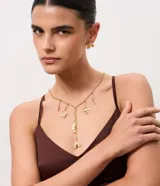 Conjunto de bijouterie compuesto por collar estilo corbata con cadena fina y dijes colgantes de pétalos texturizados, acompañado de caravanas en forma de botón con el mismo diseño.