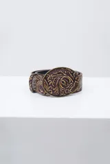 Cinto de cuero marrón con diseño grabado en relieve de estilo floral y hebilla ovalada metálica con el mismo motivo.