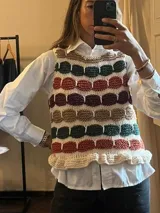 Chaleco tejido de punto sin mangas con diseño de bloques de colores horizontales en tonos tierra, verde y bordó, con detalle de volado en el ruedo.