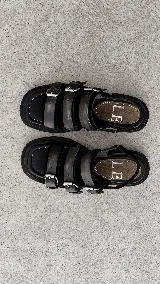 Sandalias de cuero negro con punta semicuadrada, taco cuadrado bajo y tres tiras frontales con hebillas metálicas plateadas. Cuentan con tira trasera con cierre ajustable.