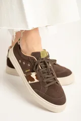 Zapatillas bajas de gamuza color marrón con cordones y suela de goma color crema. Presentan una franja lateral con estampado de vaca y el logo de la marca bordado en el lateral.