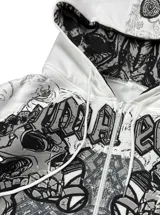 Campera con capucha color blanco, cierre frontal completo y bolsillos tipo canguro. Presenta un diseño estampado en serigrafía y DTG con calaveras y motivos ornamentales en tonos grises y negros, además de forro interior estampado en la capucha y corte oversize.