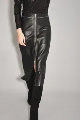 Falda midi de cuero ovino color negro, con diseño de tiro alto y cierre frontal completo con cremallera metálica. Presenta detalles de tachas decorativas a lo largo de la costura central y el borde del cierre.