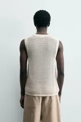 Chaleco de punto color blanco roto, con cuello redondo y sisa, confeccionado en tejido calado de estructura abierta y acabado en rib.