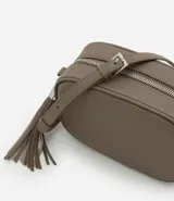 Cartera bandolera pequeña de diseño estructurado en color topo, con cierre de cremallera metálico y detalle de borla larga colgante. Cuenta con correa ajustable y forro interior.