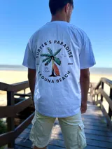 Remera celeste de corte oversize, con estampa en la espalda con diseño de palmera, tabla de surf y la inscripción 'Surfer's Paradise Laguna Beach'.