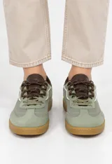 Zapatilla deportiva estilo urbano de corte bajo, color verde con suela de goma marrón y cordones oscuros.