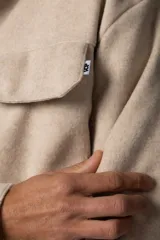 Campera corta tipo sobrecamisa de paño elastizado en color beige, con cuello clásico, cierre frontal de botones veteados y dos bolsillos frontales con tapa.