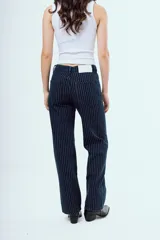 Pantalón de jean azul oscuro de corte recto y tiro medio, con diseño de rayas diplomáticas blancas. Presenta bolsillos delanteros y traseros, y cierre frontal con botón y cremallera.
