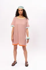 Vestido corto tejido de punto color salmón, con cuello redondo y mangas cortas. Presenta ribetes en color amarillo en el cuello, celeste en las mangas y naranja en el ruedo.