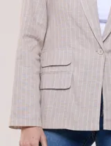 Blazer de lino y algodón color beige con diseño de rayas diplomáticas blancas, solapa clásica, cierre de un botón frontal y bolsillos laterales con solapa.