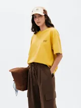 Camiseta de corte oversized color amarillo, con cuello redondo, mangas cortas y estampa pequeña en el pecho con el texto (DESDE) 18-80.