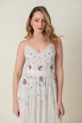 Vestido midi de tul color marfil con escote en V y tirantes finos. El corpiño y la falda están adornados con lentejuelas y apliques bordados en tonos pastel como lila, rosa y azul, simulando flores. La falda es voluminosa y con capas de tul.