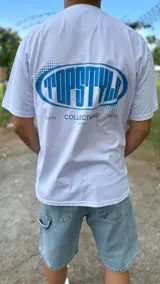 Remera blanca oversize de manga corta, con estampa azul en la espalda con el texto 'TOP STYLE COLLECTIONS'.