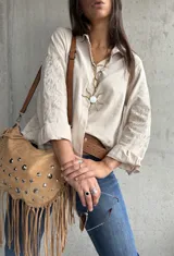 Camisa de color beige con cuello clásico, cierre frontal de botones y mangas largas con puños doblados. Presenta un delicado bordado floral en las mangas.