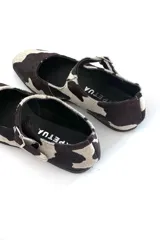 Zapato Mary Jane con estampado de vaca en blanco y negro, con correa al tobillo y hebilla plateada.