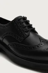 Zapato de vestir tipo brogue negro, con detalles de perforaciones decorativas y suela track dentada.