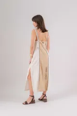 Vestido largo de lino con diseño bicolor en beige y crudo, escote en V y breteles regulables. Presenta detalles de bordados geométricos en el frente y tajos laterales.