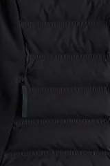 Campera deportiva negra híbrida con cuerpo acolchado y mangas de tejido elástico. Presenta cuello alto, cierre frontal con protección para el mentón, bolsillos laterales y bolsillos interiores.