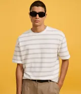 Remera de corte boxy con cuello redondo y mangas cortas. Presenta un diseño de rayas horizontales finas en tonos gris sobre fondo blanco.