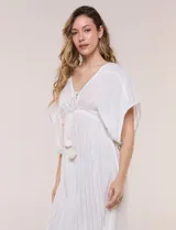 Vestido largo blanco confeccionado en viscosa con hilos de lurex, escote en V profundo con lazo y borlas, mangas kimono y falda fluida con volados en el ruedo.