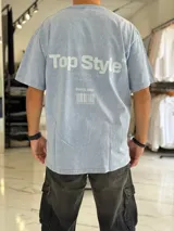 Remera oversize de efecto gastado color celeste, con cuello redondo y mangas cortas. Estampado frontal pequeño con el texto "Top Style" y gran estampado en la espalda con el mismo texto, la frase "Dream big. Work hard. Make it real.", el año "SINCE 2021" y un código de barras.