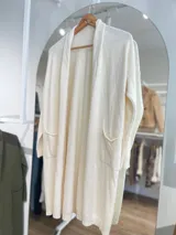 Saco largo color crema, de tejido de punto, con bolsillos laterales y corte recto.