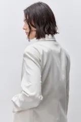 Blazer de silueta amplia y largo por debajo de la cadera, color marfil, confeccionado en tela suave y liviana. Presenta cuello con solapas, hombreras, manga larga y cierre cruzado con botones carey.