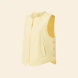 Chaleco acolchado sin mangas en color amarillo pastel, con cierre frontal de cremallera y botones a presión en los laterales. Presenta un diseño minimalista con cuello redondo y bolsillos frontales integrados.