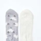 Pack de dos pares de medias de tejido suave y afelpado. Un par es de color gris con estampado de corazones blancos y antideslizante en la planta, y el otro par es de color blanco liso con un pequeño corazón bordado.