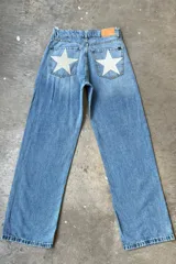 Jean de mezclilla celeste, corte holgado o recto, con grandes estrellas estampadas en color blanco o gris claro en los bolsillos traseros. Tiene un parche de cuero marrón en la cintura trasera con el logo de la marca.