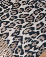 Bufanda de gran tamaño con estampado animal print en tonos negro y beige, con terminación de flecos en los extremos.