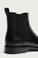 Bota estilo Chelsea de color negro, con parte superior lisa, paneles elásticos laterales y tirador trasero. Cuenta con horma redonda y suela con ligero tacón.