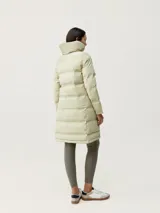 Campera larga tipo puffer de color beige, con acabado mate, cuello alto envolvente y cierre frontal con cremallera. Presenta diseño de bandas acolchadas termoselladas, bolsillos laterales con cierre oculto y relleno vegano.