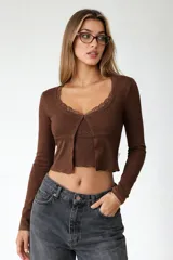 Conjunto de dos piezas compuesto por un cardigan de manga larga con detalle de encaje en el cuello y un top de tirantes con escote en V y detalle de encaje. Ambas prendas son de color marrón y presentan un diseño ajustado con terminaciones onduladas.