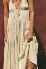 Vestido largo color crudo de tela satinada, con escote en V, tirantes finos ajustables, detalle de cordón ajustable en el pecho y diseño fruncido en capas.