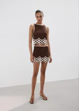 Falda corta de tejido crochet color marrón con detalles de flores blancas en el borde inferior. Silueta recta y forro interior.